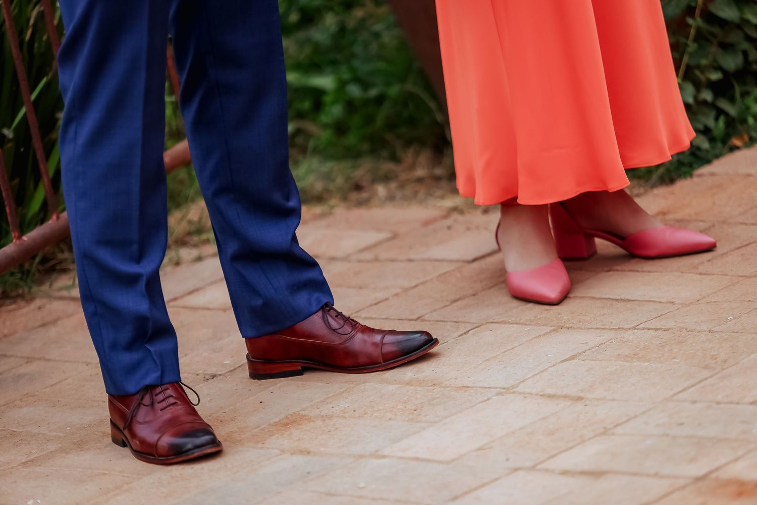Close-up of groom in blue suit with brown oxford shoes standing beside woman in coral dress.