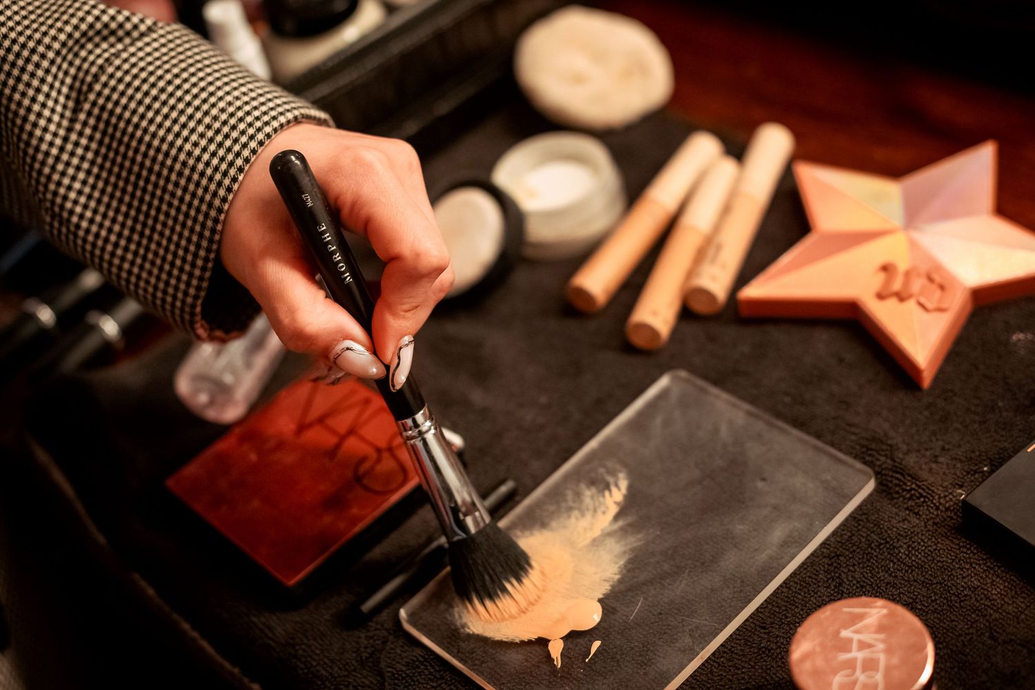 Makeup artist applying foundation with brush on palette surrounded by cosmetics and tools.