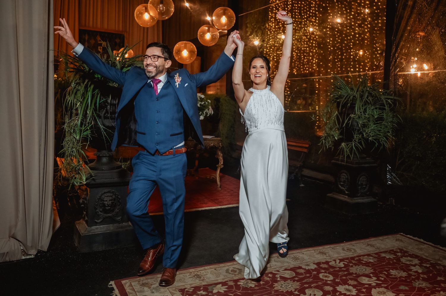 Joyful bride and groom making a grand entrance at their wedding reception under warm string lights.