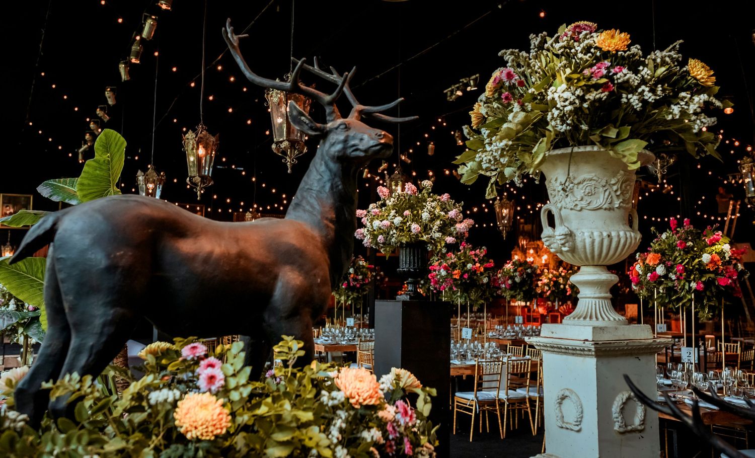 Bronze deer statue surrounded by colorful floral arrangements in a dramatic wedding reception venue.