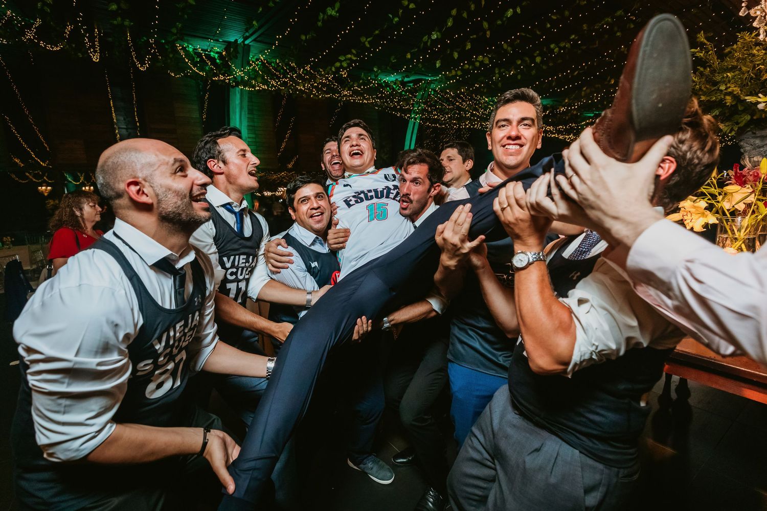 Groomsmen in Vieja Escuela jerseys lifting and carrying guest at fun wedding reception party.