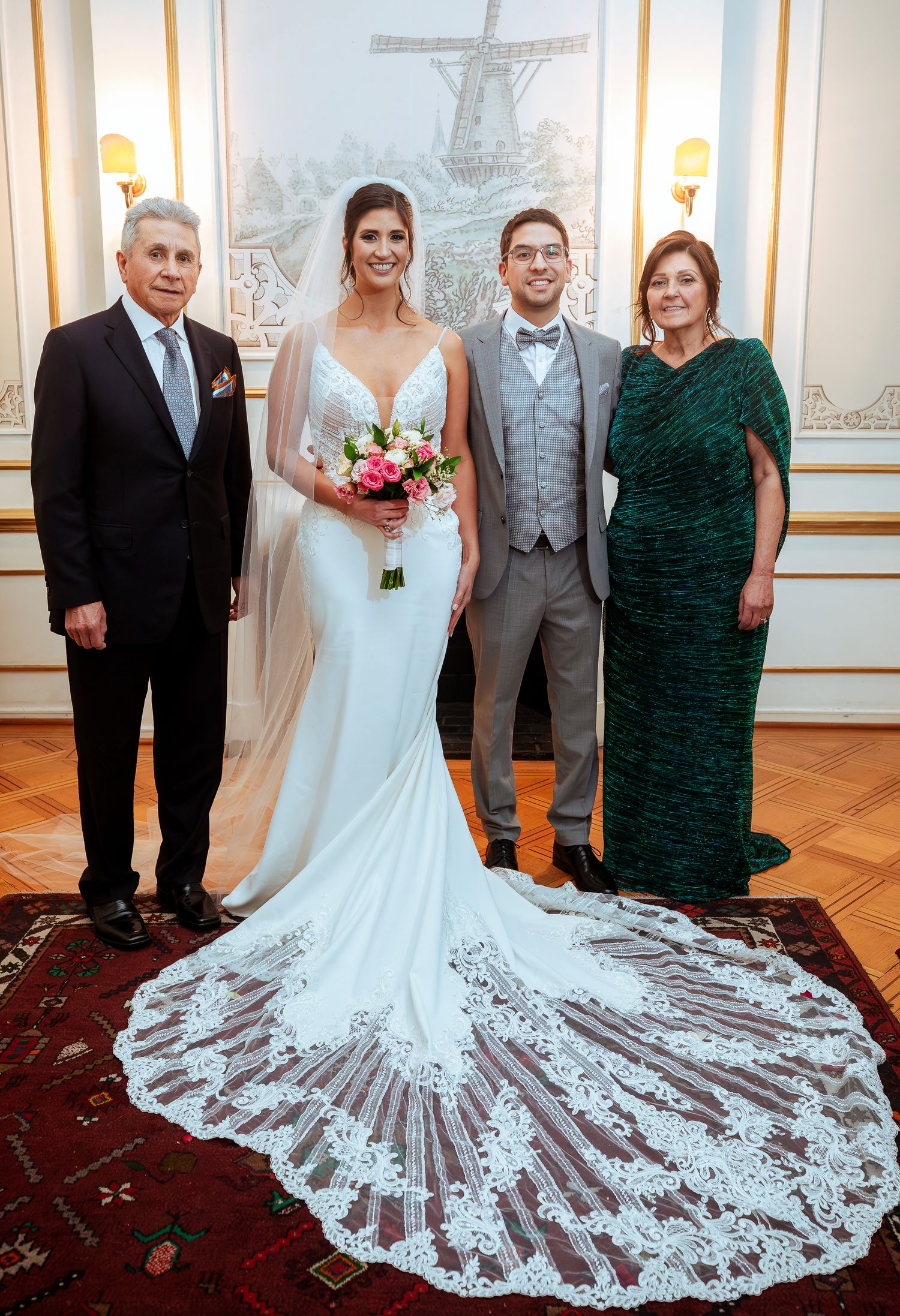 Bride in white gown with lace train poses with groom in gray suit and family members at elegant wedding venue.