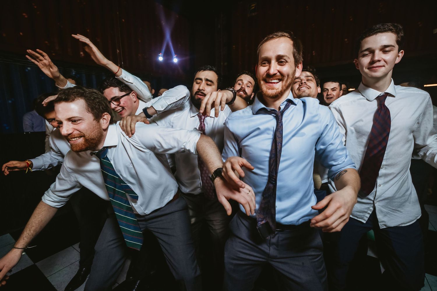 Group of young men in dress shirts and ties dancing and celebrating at a formal party or wedding reception.