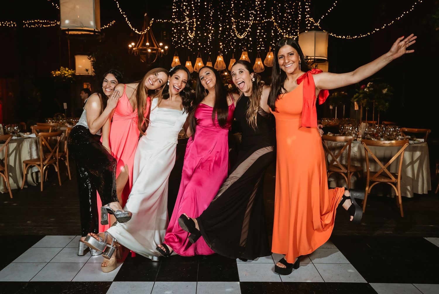 Bride in white gown celebrates with bridesmaids in colorful dresses on dance floor at wedding reception.