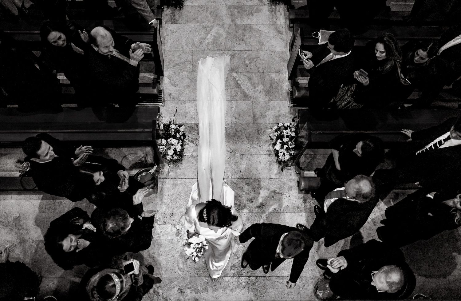 Aerial black and white photo of a bride walking down the church aisle surrounded by wedding guests.