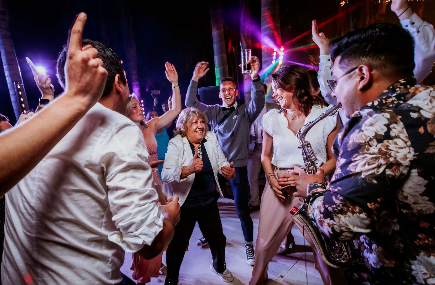 Energetic wedding guests dancing together under colorful lights at reception party.