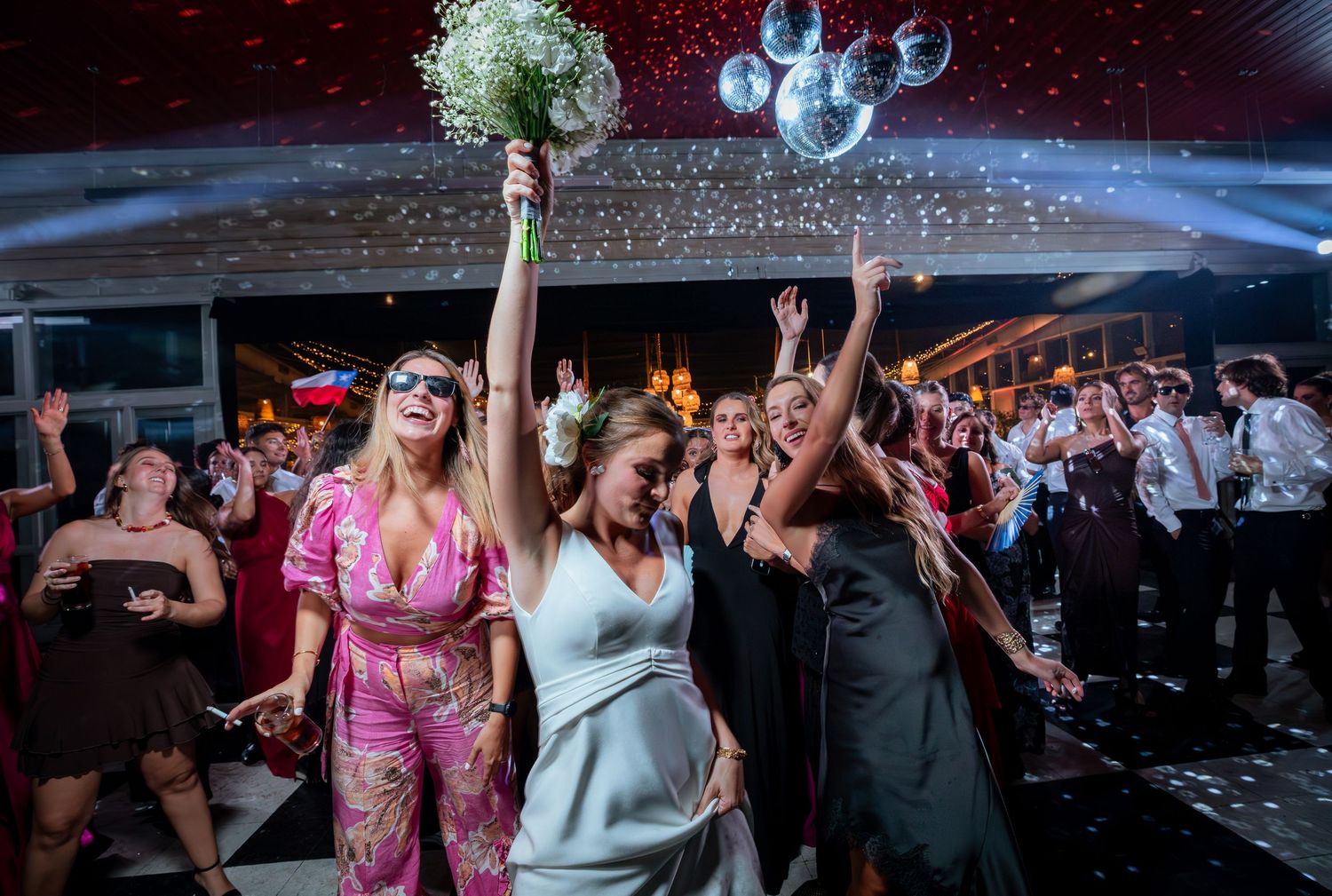 Bride tossing bouquet with excited guests reaching up at elegant wedding reception.