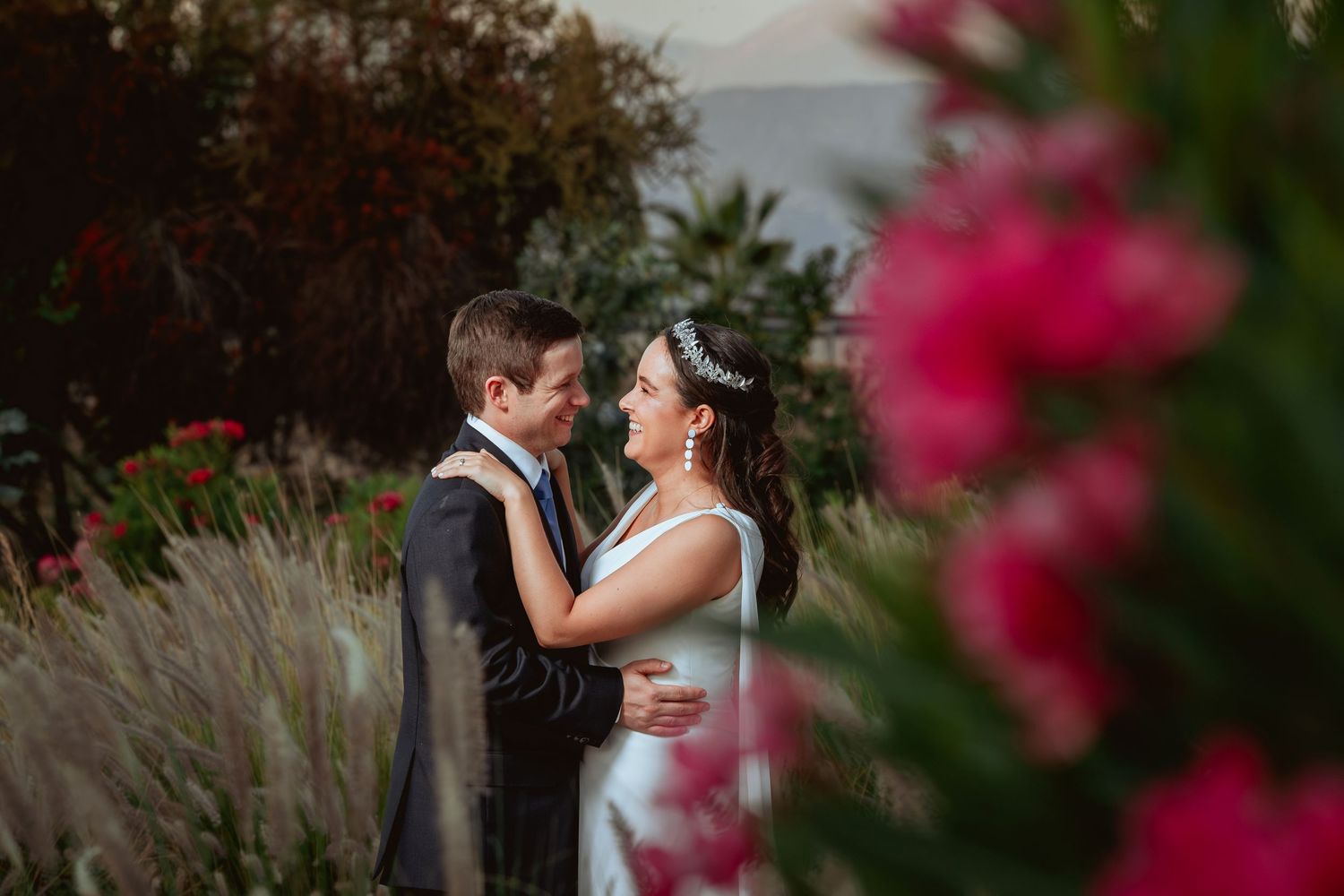 Wedding couple embracing romantically with vibrant pink flowers framing the foreground.