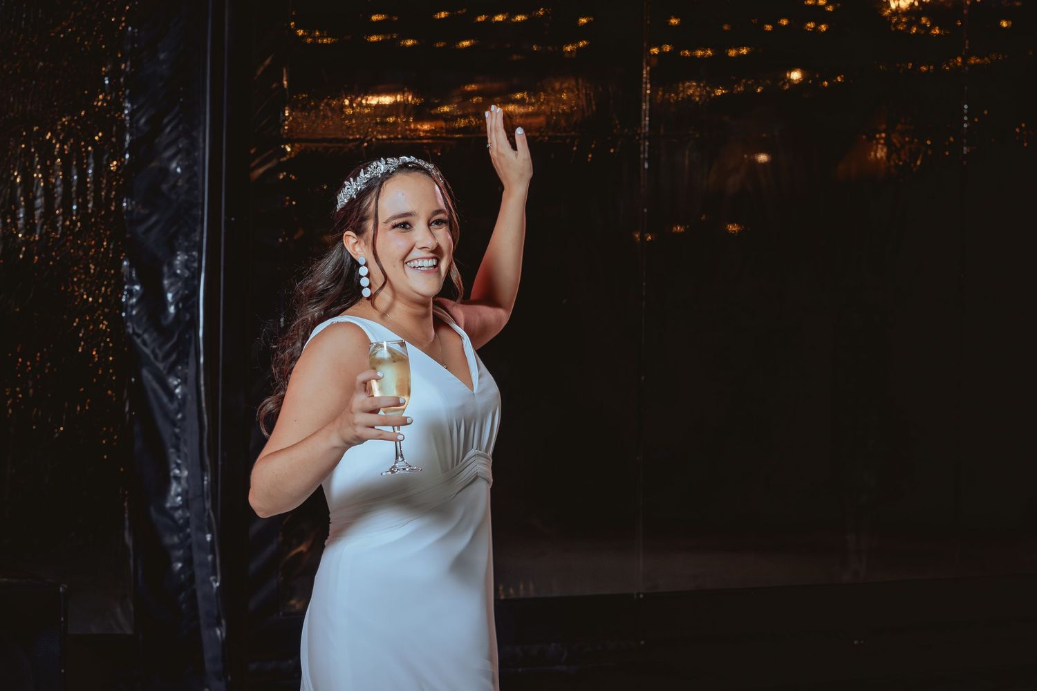Smiling bride in white gown holding champagne glass at her wedding reception.
