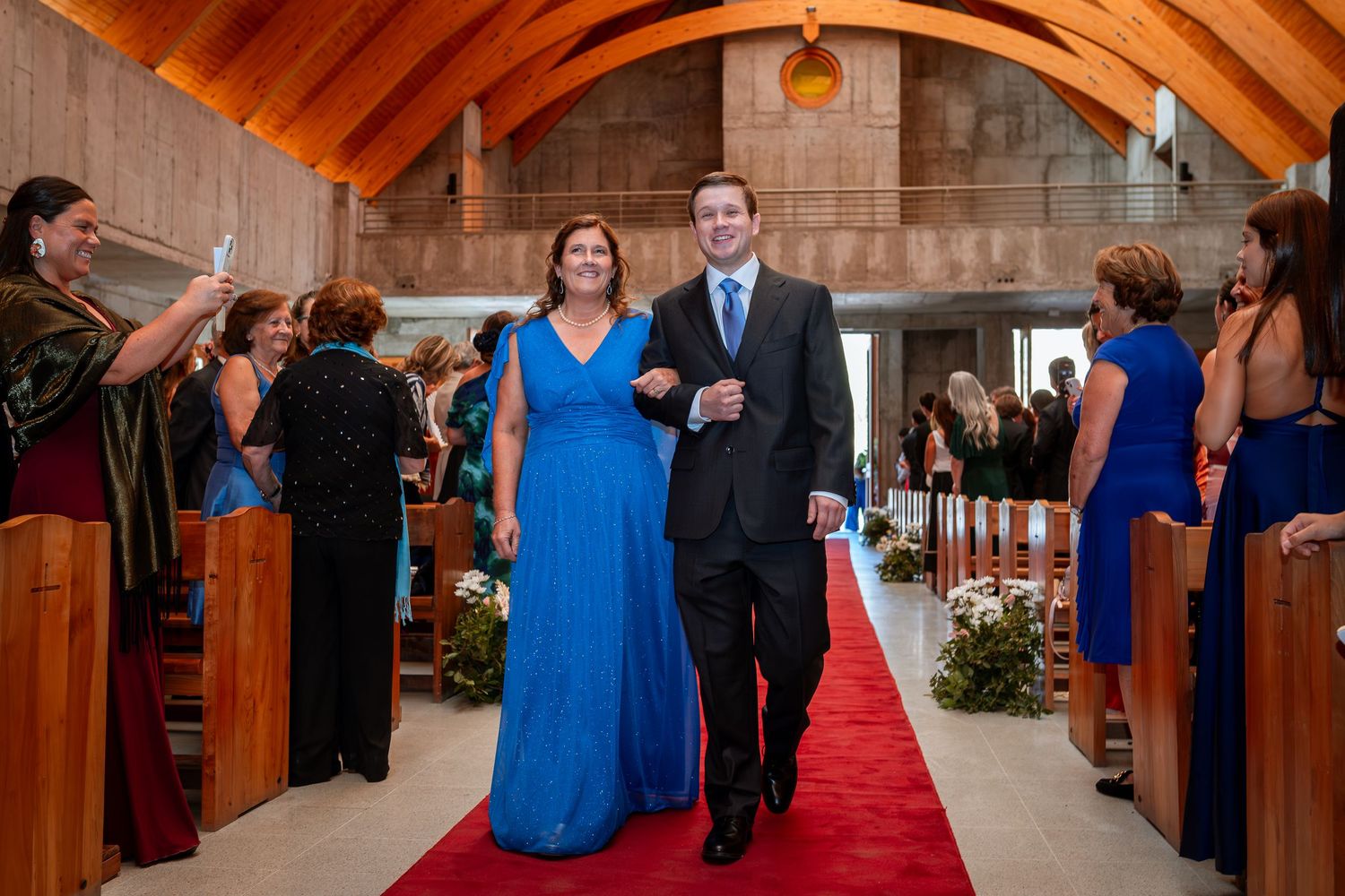 Bride in blue gown walks down red carpet aisle with escort in church wedding.