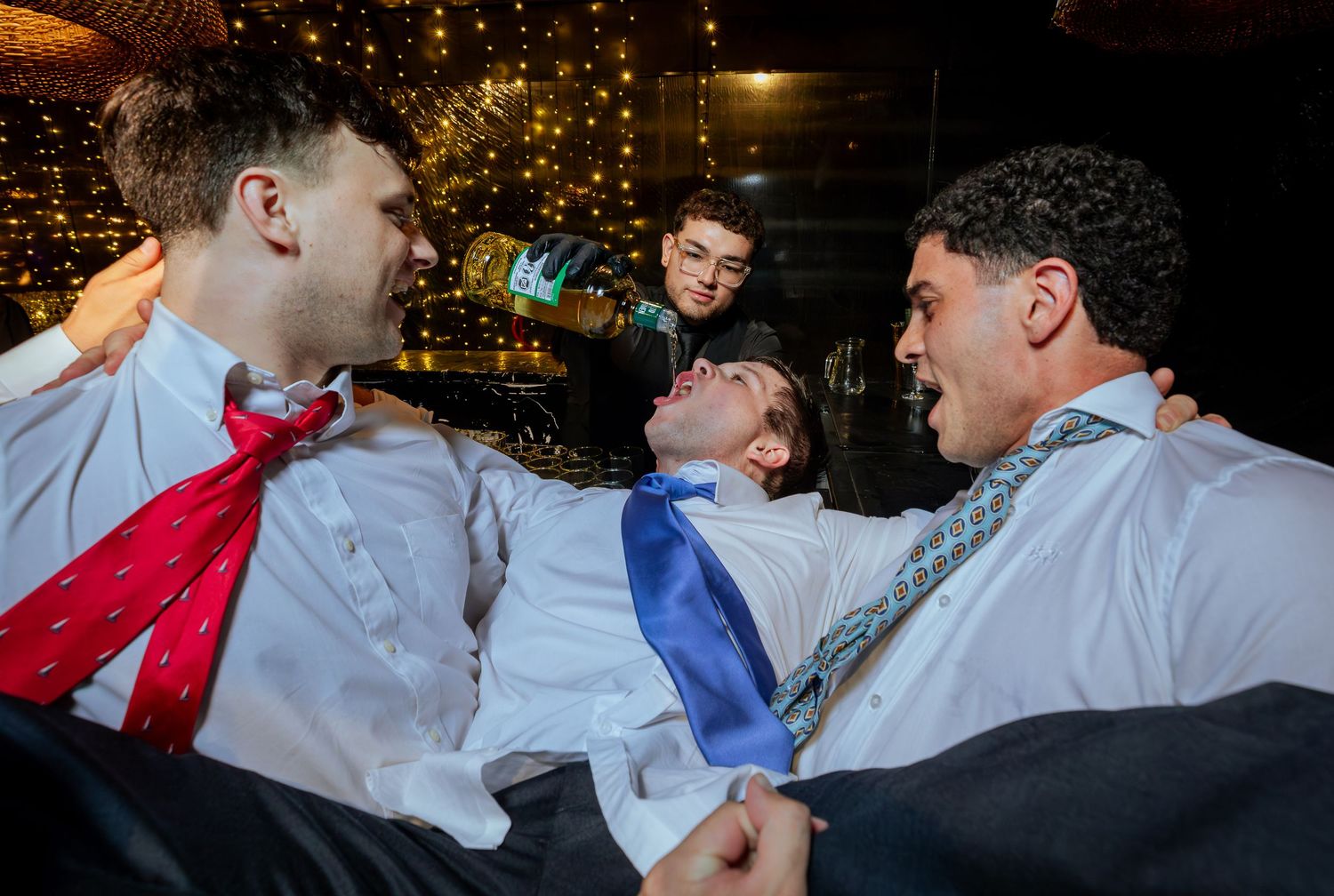 Three young men in dress shirts and ties laughing together at a wedding reception party.