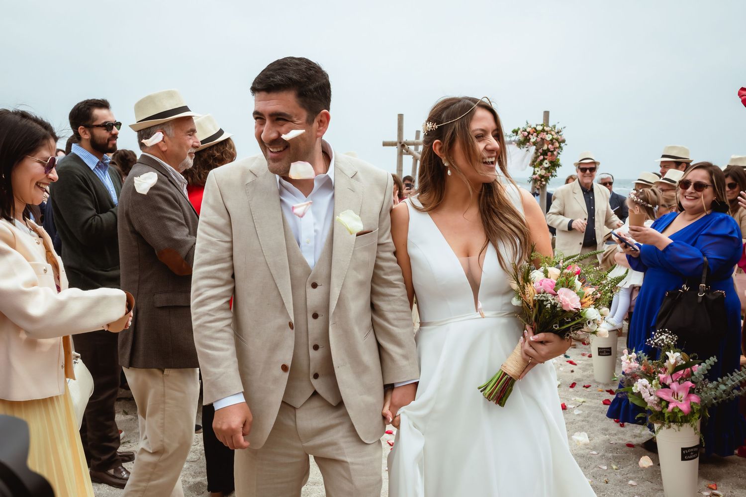Smiling bride and groom walk together after their outdoor beach wedding ceremony with guests celebrating.