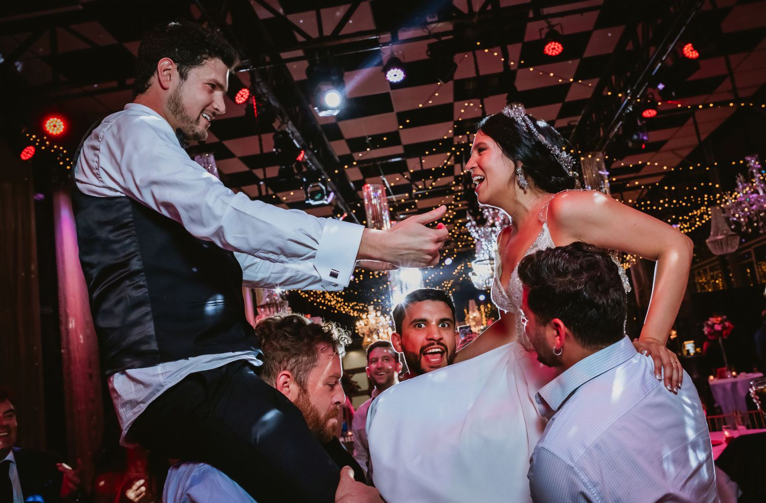 Bride and groom being lifted by guests on shoulders during a festive wedding reception.