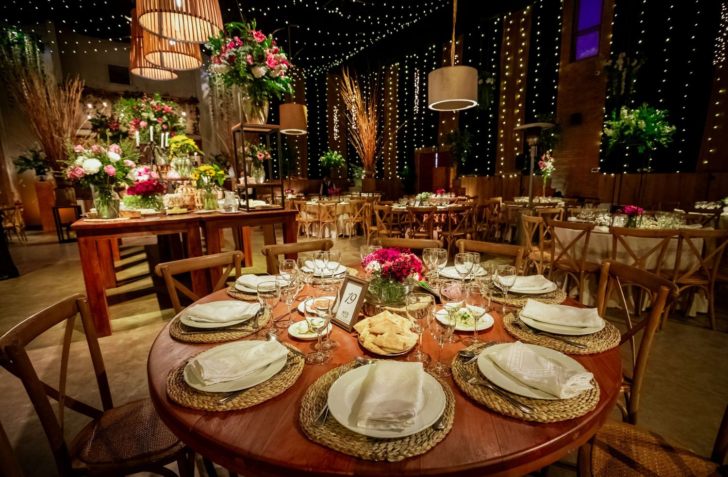 Rustic wedding reception table with golden charger plates, white napkins, and pink floral centerpieces.
