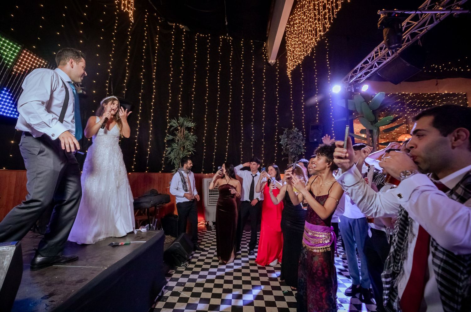 Bride and groom performing on stage while guests clap and cheer at a vibrant wedding reception.