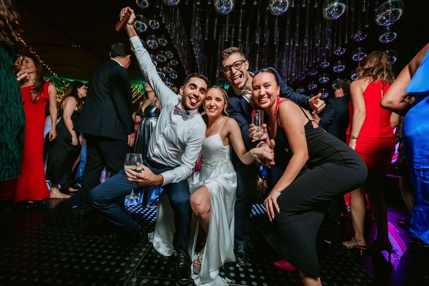 Excited wedding guests celebrate with bride on dance floor at lively disco-themed wedding reception.