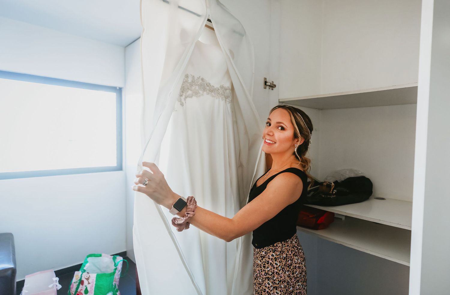 Smiling bride admiring her white wedding dress hanging in a closet.