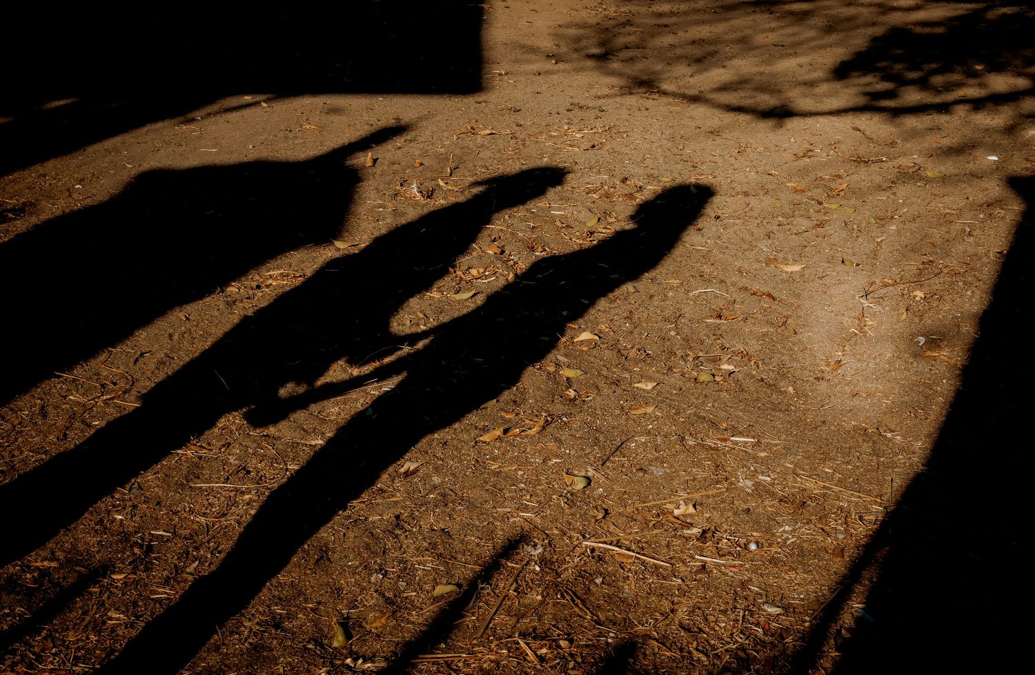 Long shadows of two people cast across dry dirt ground in warm golden light.