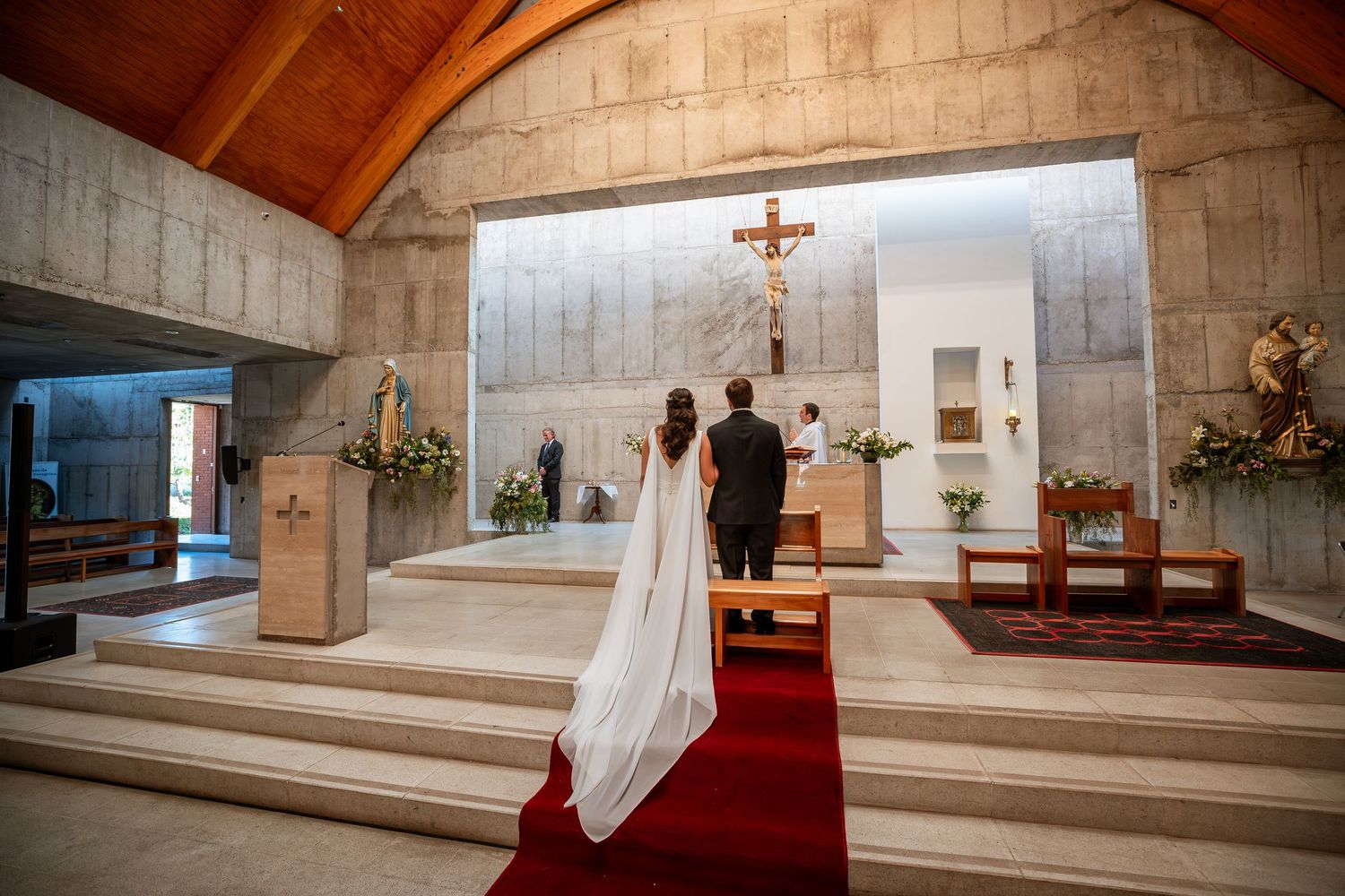 Bride and groom stand before altar in modern concrete church during wedding ceremony.