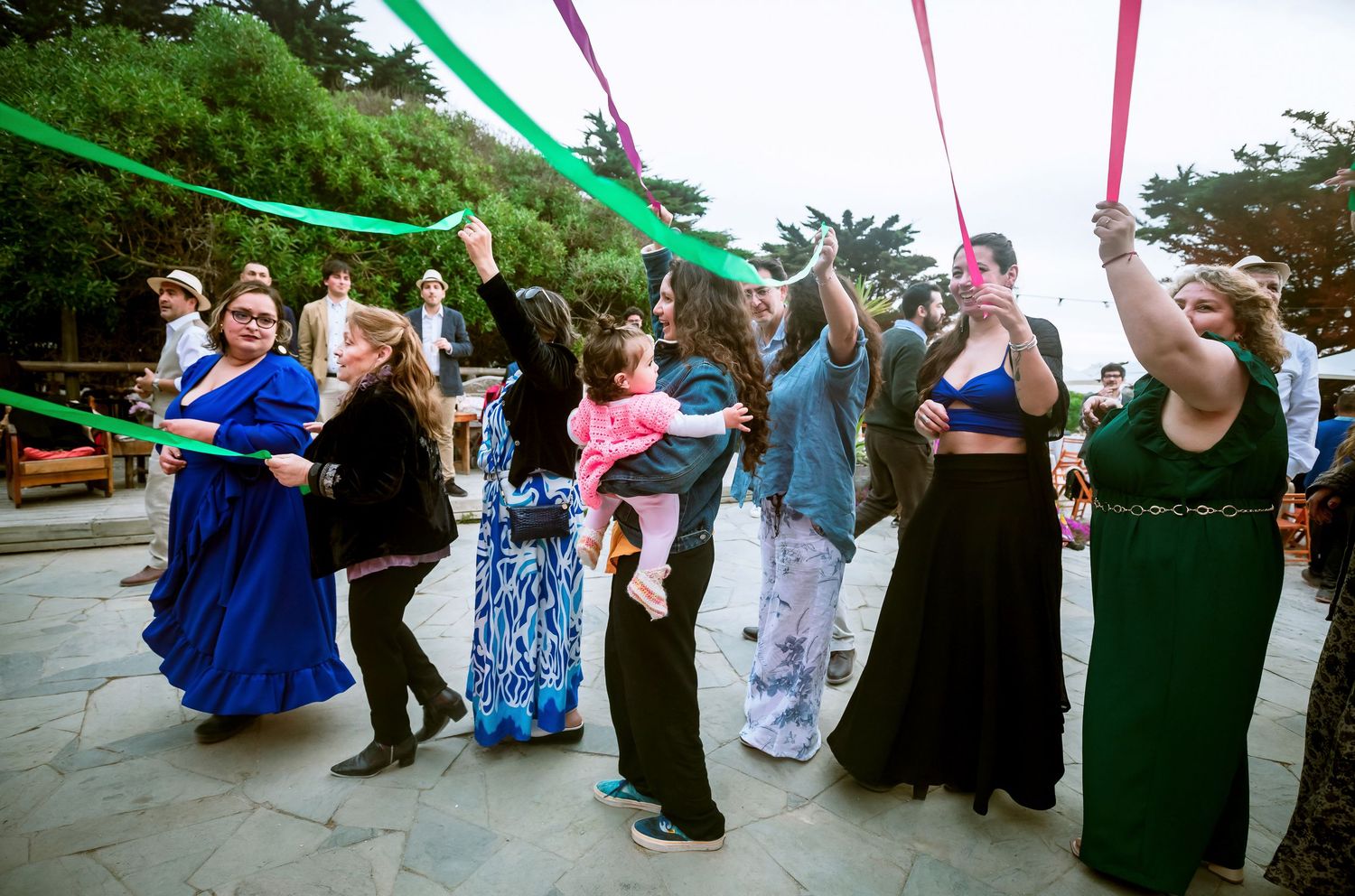 Wedding guests dance joyfully with colorful streamers during lively outdoor reception celebration.