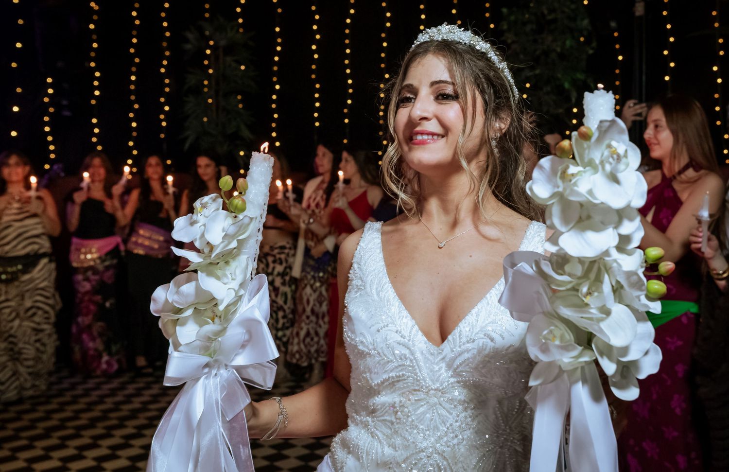 Radiant bride holding white orchid-adorned candles at an outdoor evening wedding celebration.