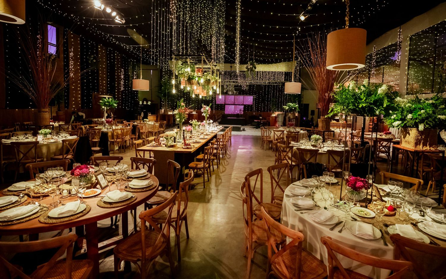 Romantic indoor wedding venue with fairy lights, wooden chairs, and lush floral centerpieces.