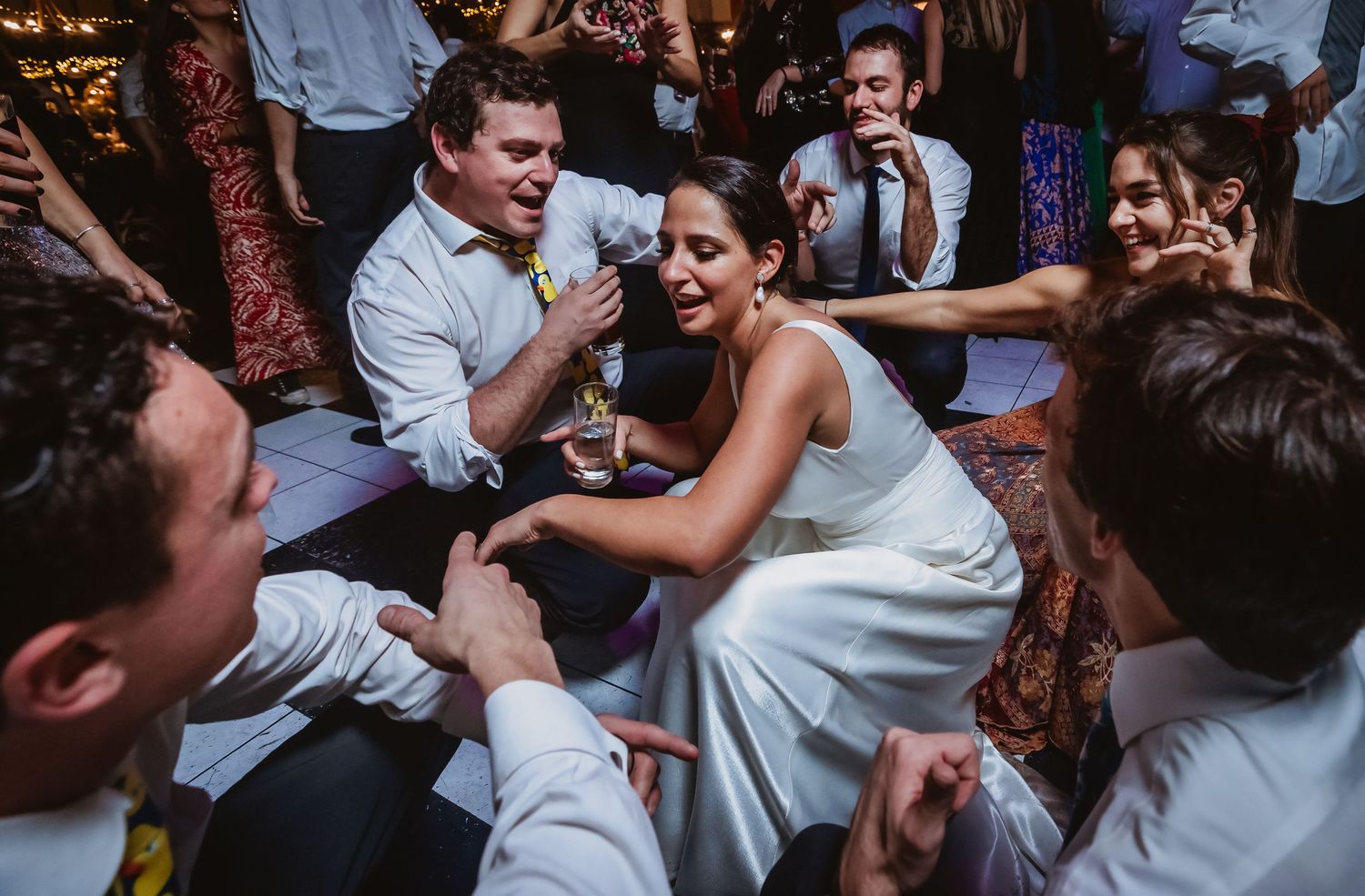 Bride in white dress laughing and dancing with guests on the wedding reception dance floor.