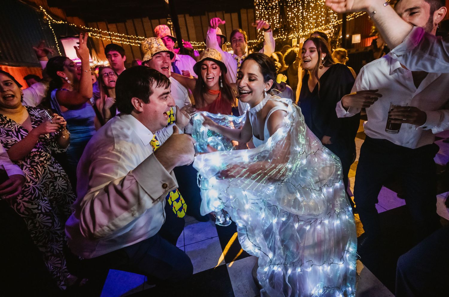 Bride in LED light dress dancing joyfully with groom at lively wedding reception party.