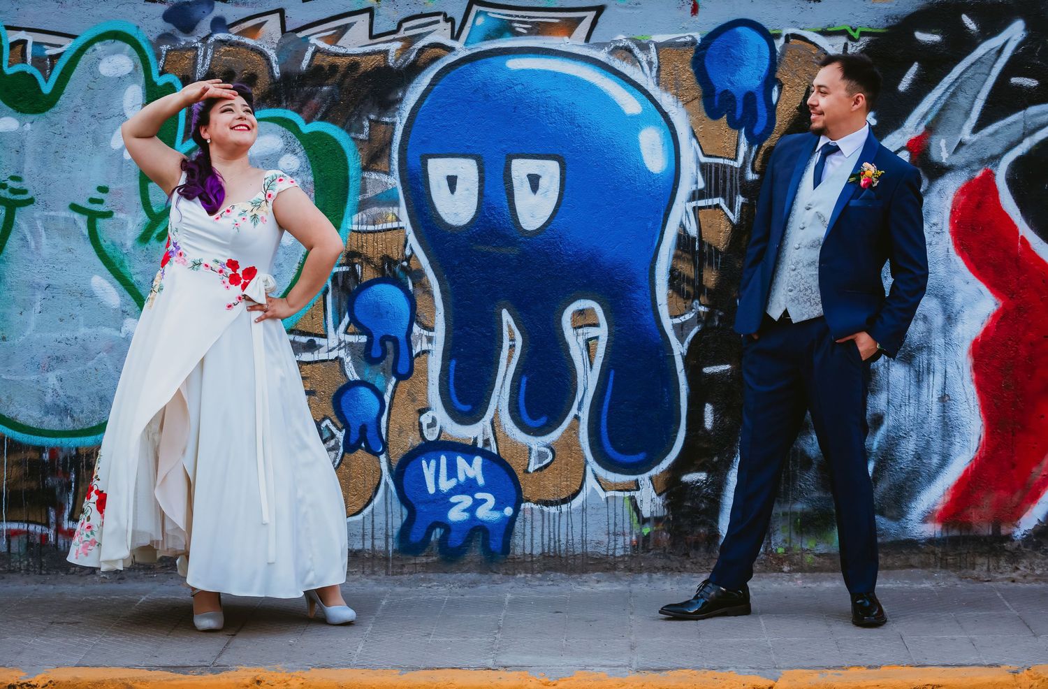 Bride and groom posing in front of colorful graffiti wall featuring blue octopus street art at urban wedding.
