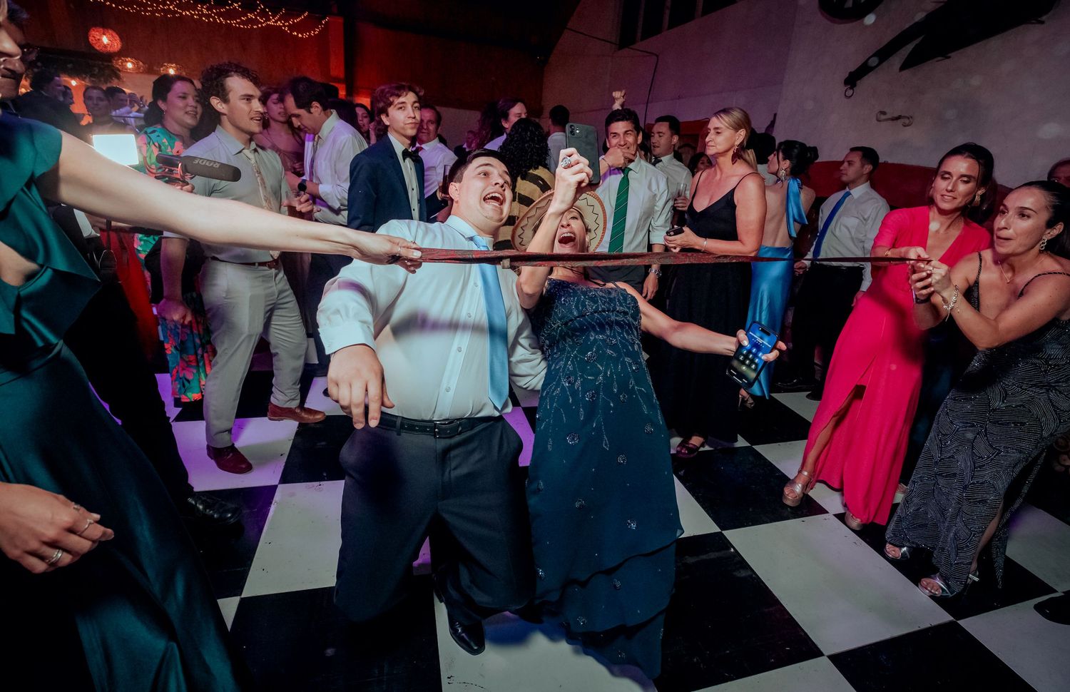 Wedding guest does limbo dance under bar while crowd cheers at festive reception celebration.