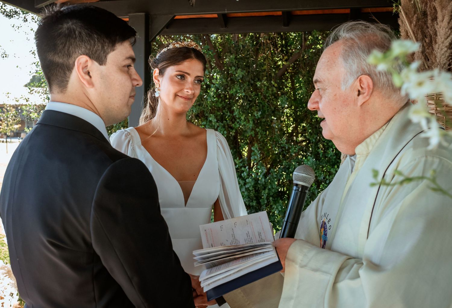 Groom and bride exchange vows with officiant reading from a book at an intimate outdoor wedding ceremony.