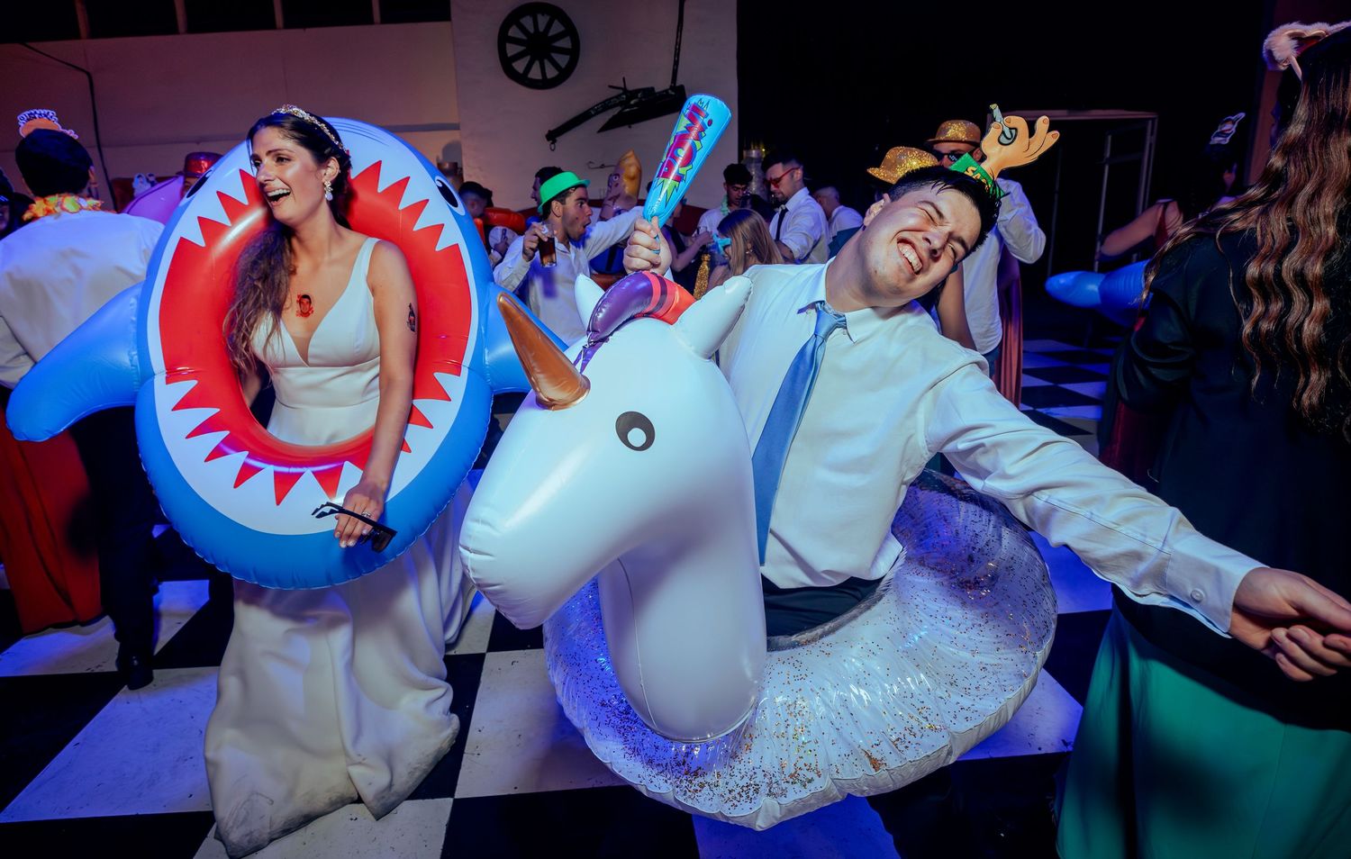 Bride and groom laughing with inflatable shark and unicorn floats at wedding.