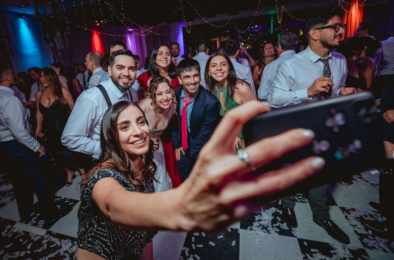 Wedding guests take a group selfie on the dance floor during a lively wedding reception celebration.