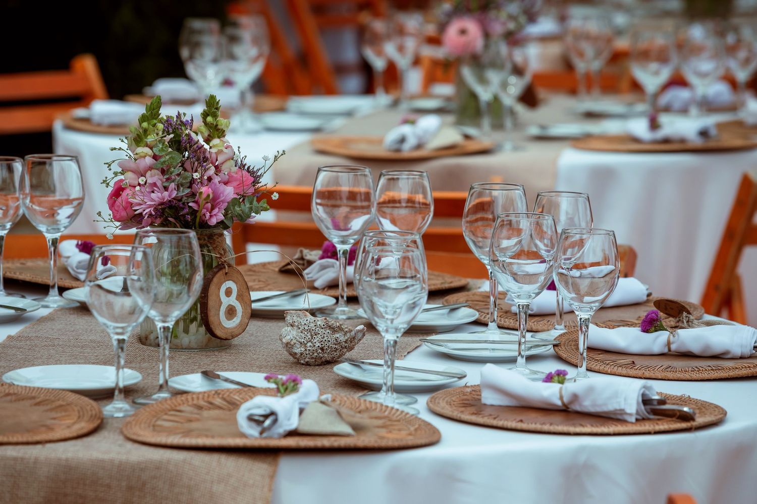 Elegant outdoor wedding reception table with floral centerpiece, wine glasses, and burlap placemats.
