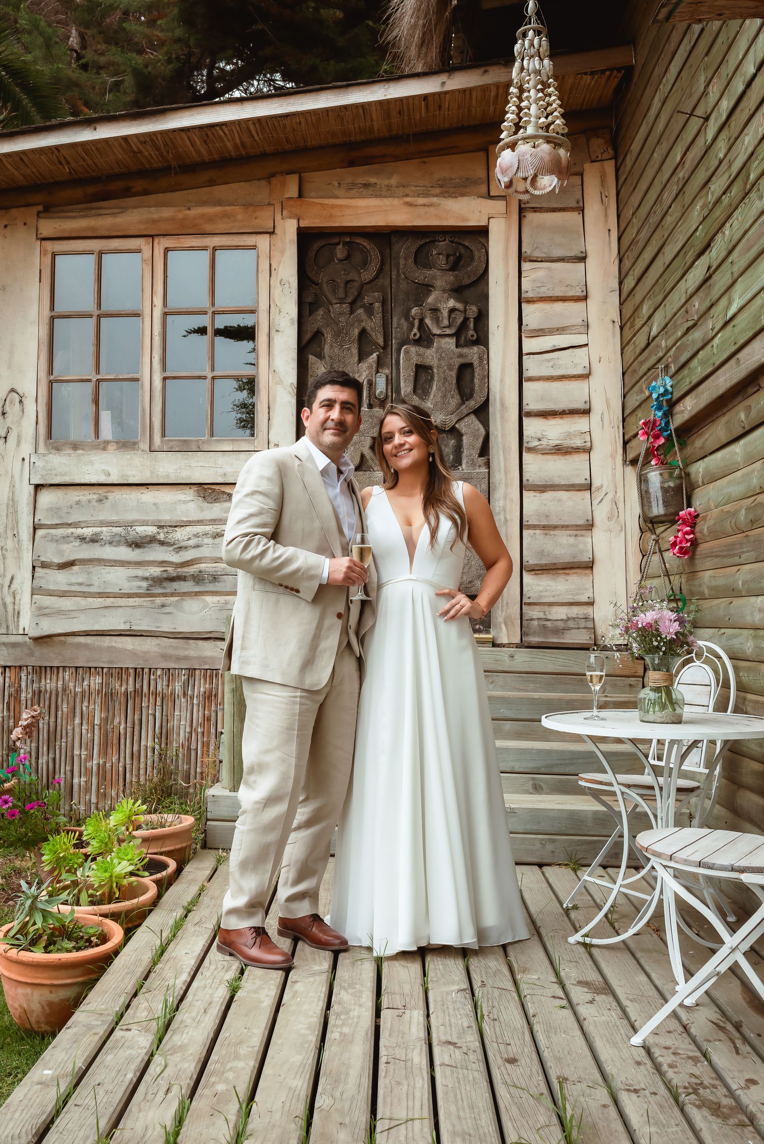 Bride and groom pose together on a rustic wooden porch in front of a charming log cabin.