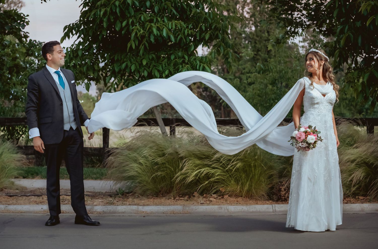 Bride and groom stand apart as her flowing white veil creates an elegant wave between them.