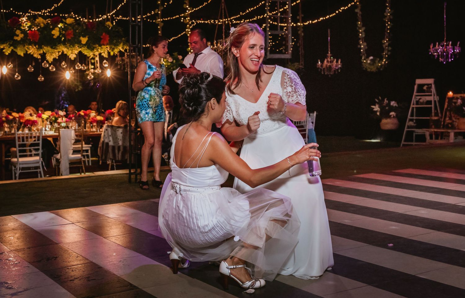 Two brides share a tender moment on a black and white dance floor at an elegant outdoor wedding reception.