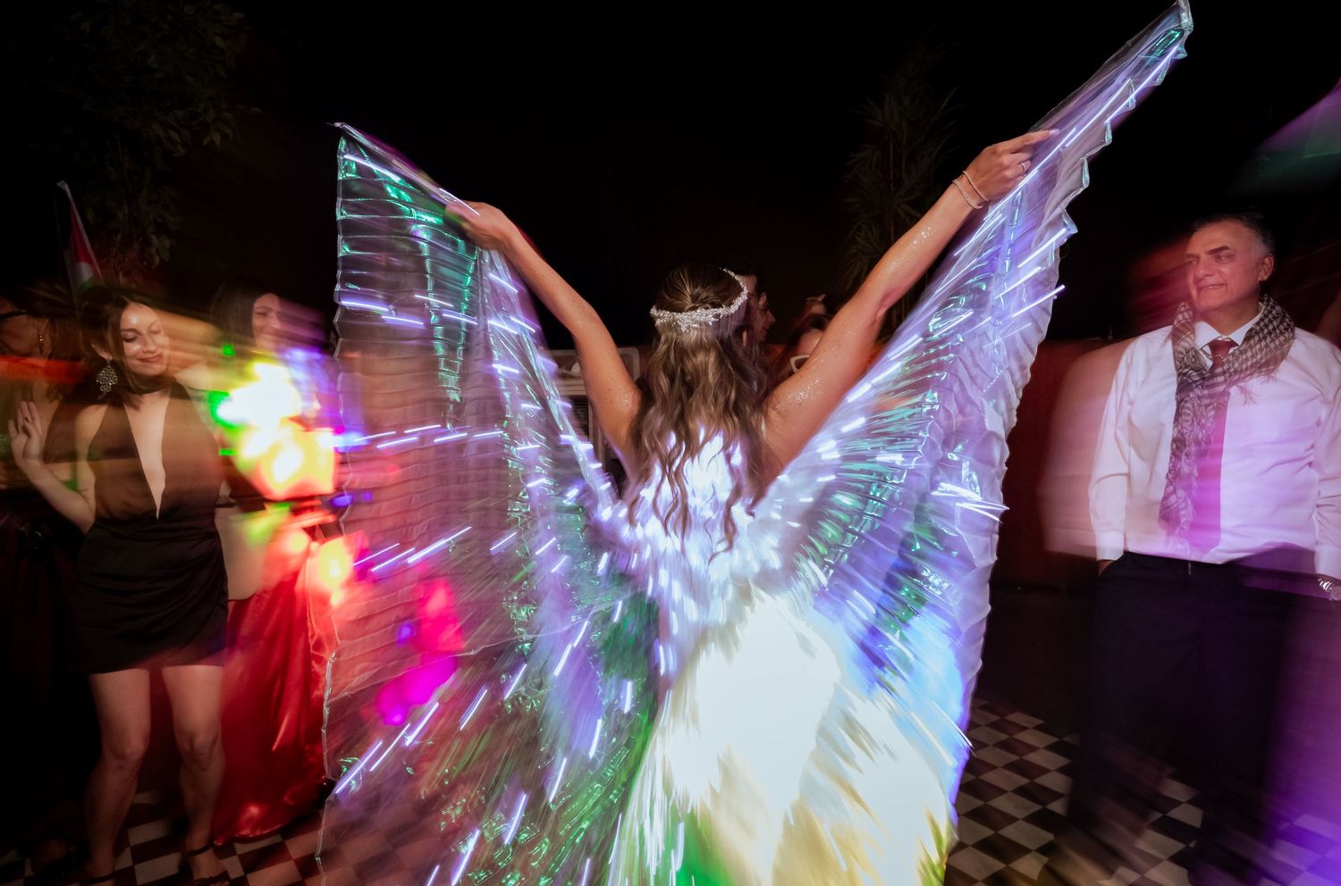 Performer with glowing LED rainbow wings dancing at an enchanting nighttime wedding reception event.