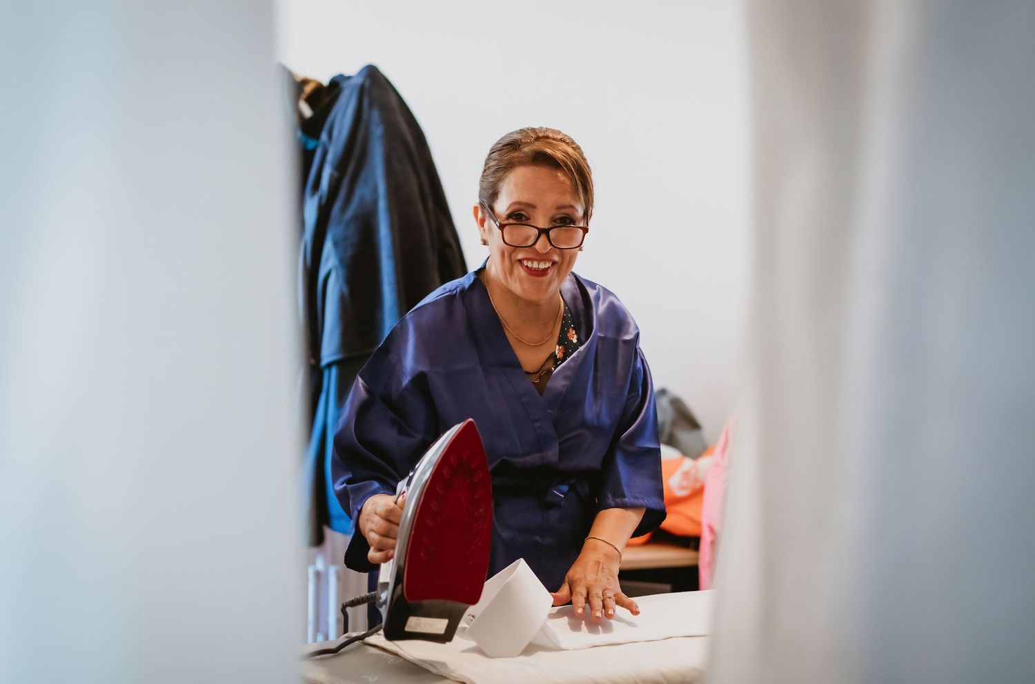 Smiling woman in blue robe ironing wedding garments in preparation for the big day.