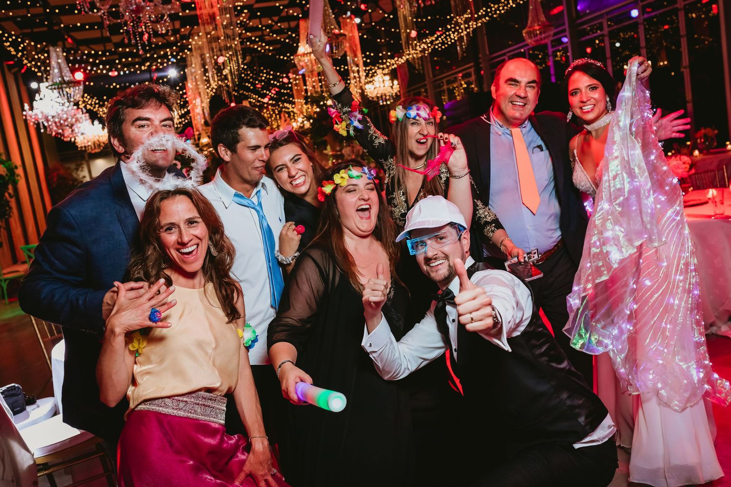Group of festive wedding guests posing and smiling at a colorfully decorated reception party.