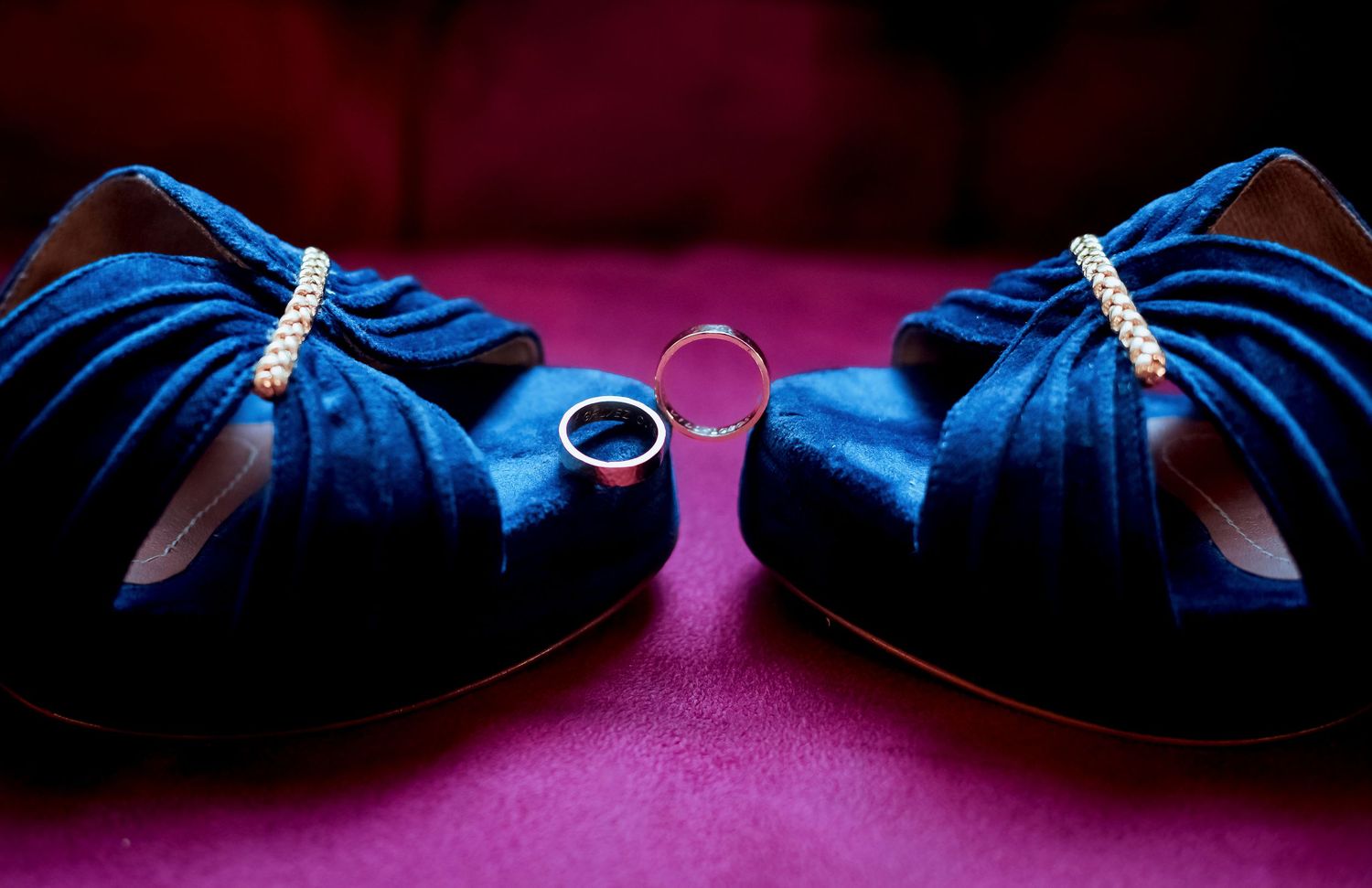 Elegant blue velvet wedding heels with pearl detail framing gold and silver wedding rings.