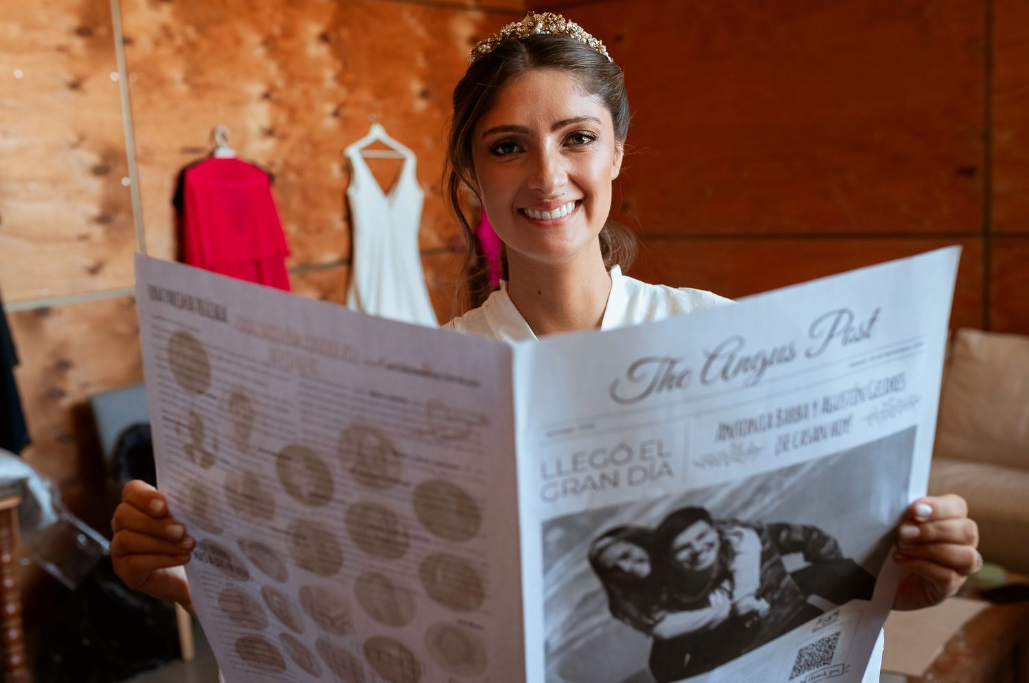 Smiling bride in a tiara reading The Angus Post wedding newspaper during bridal preparations.