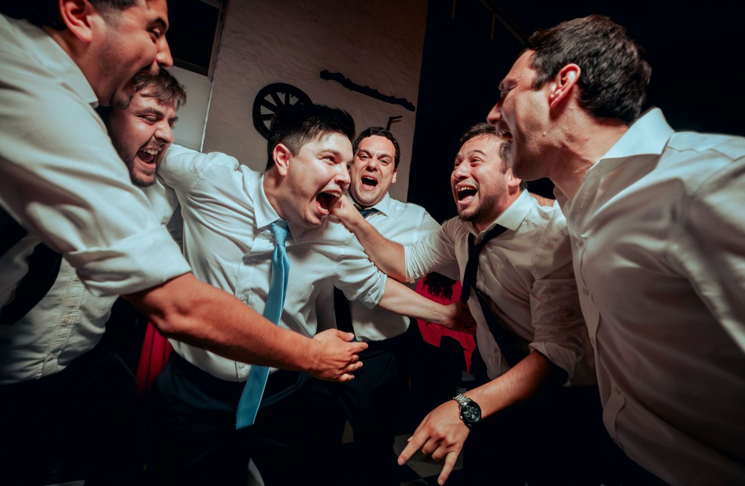 Groomsmen in white shirts celebrate joyfully together at a wedding reception party.