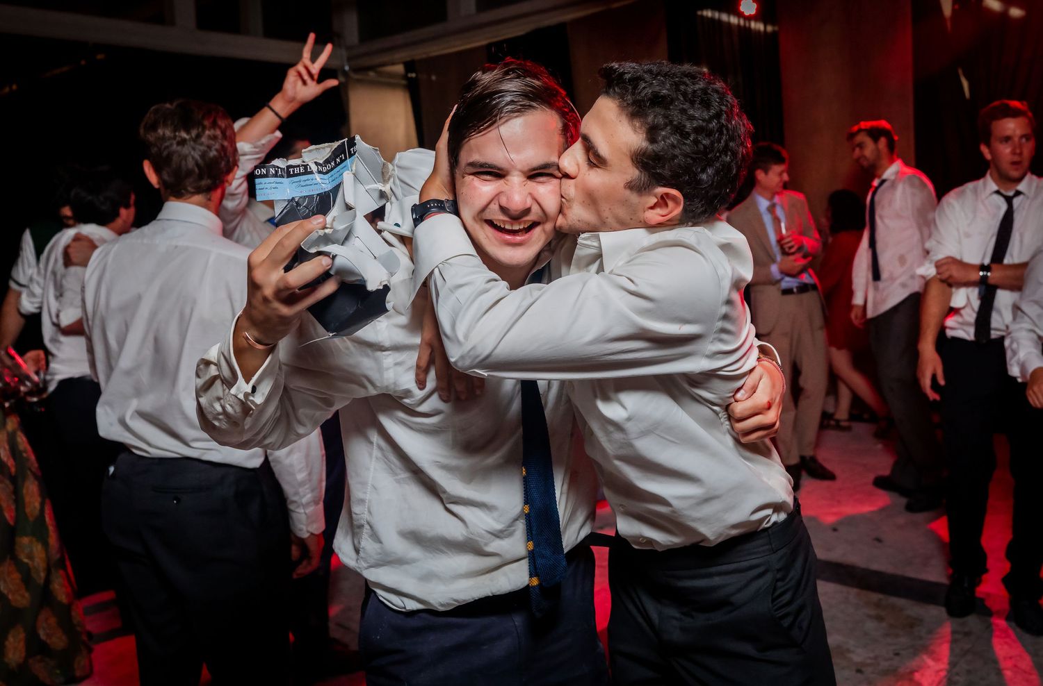 Two friends take a selfie while hugging at a vibrant wedding reception celebration.