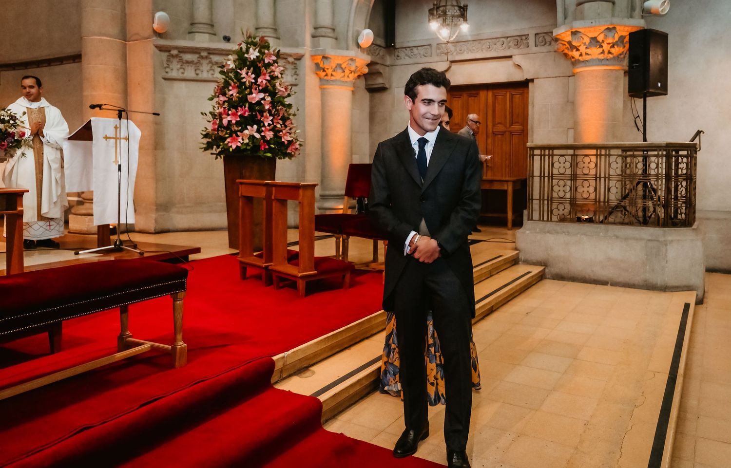 Groom in black suit standing at church altar awaiting bride during wedding ceremony.