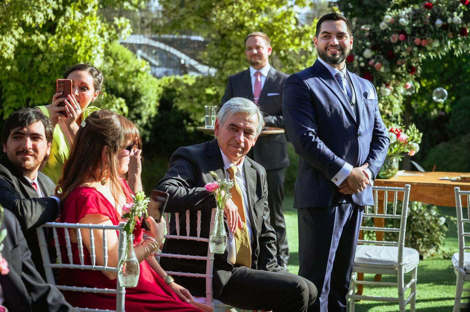 Wedding guests smile and interact in garden ceremony, man in navy suit stands prominently.