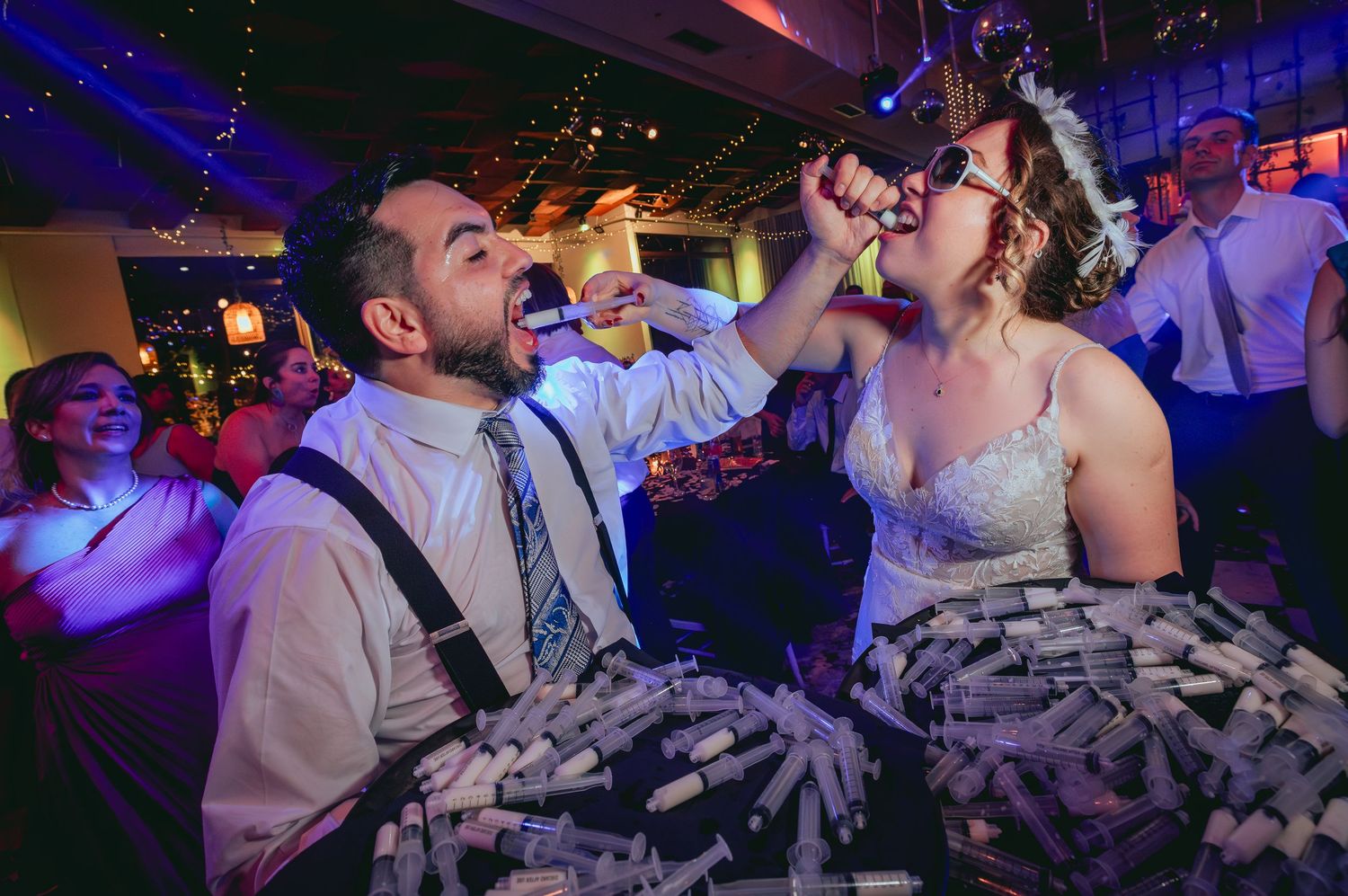 Bride and groom taking shots together at lively wedding reception with blue lighting.