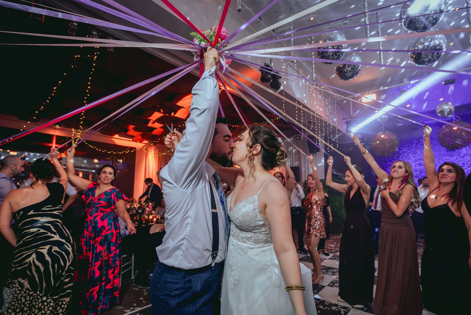 Bride and groom share a kiss under colorful streamers on the wedding dance floor.