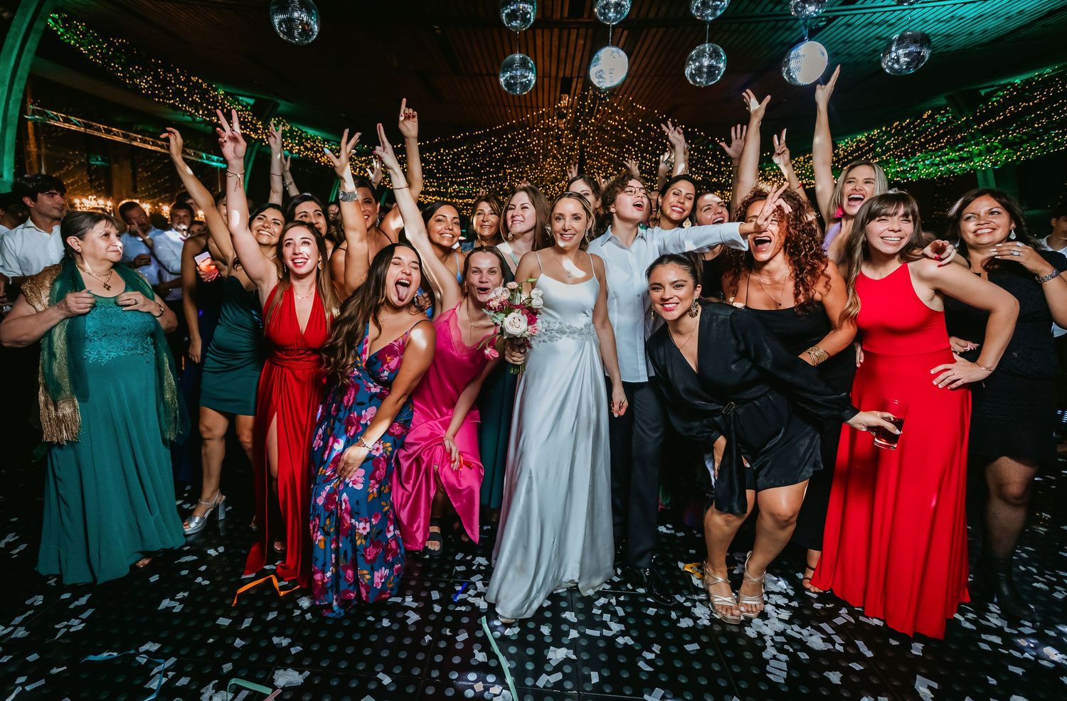 Bride poses with large group of joyful wedding guests on a decorated dance floor.