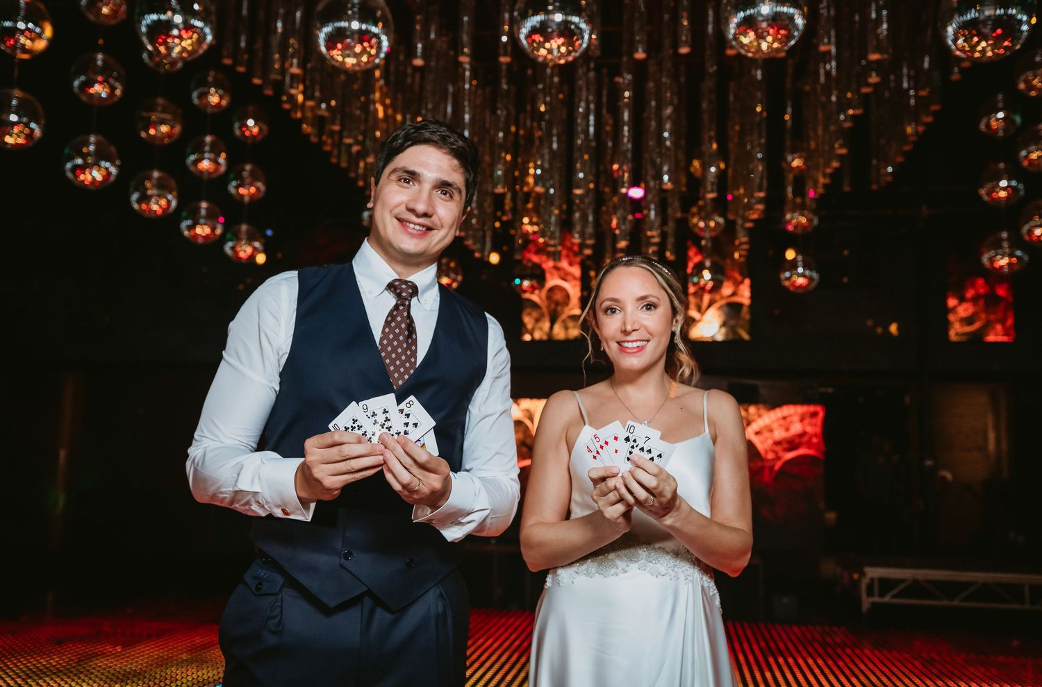 Bride and groom smiling while holding playing cards during a magic show at their wedding reception.